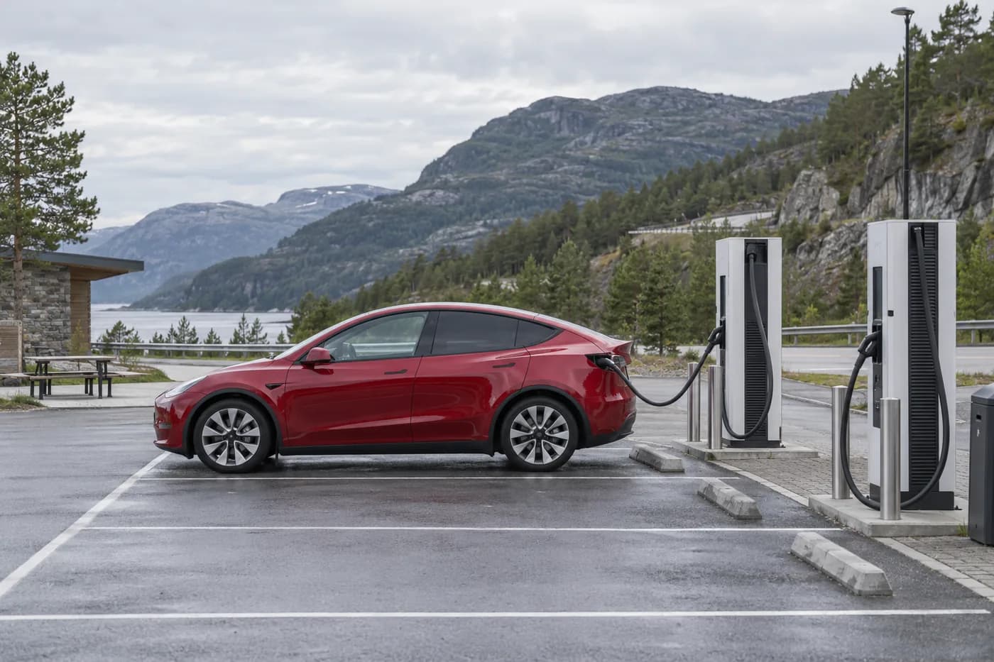 KI-illustrasjon av rød elbil ved hurtigladere i et norsk fjordlandskap